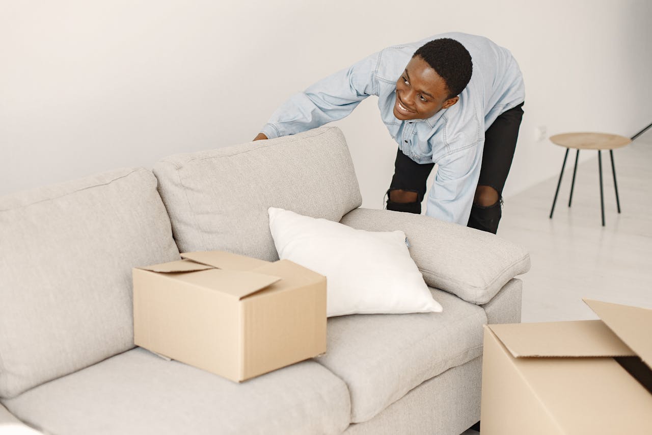 services-02 Young man smiling while arranging cardboard boxes in a modern living room.