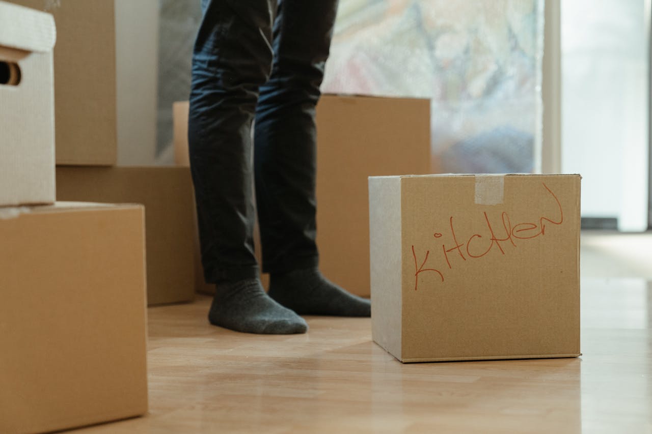 about-01 A person standing in a room surrounded by moving boxes labeled for the kitchen.